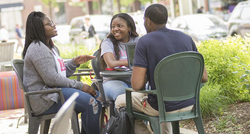 Three students sitting and laughing at a table in Up Town Normal.